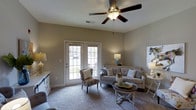 This single-story residence features two bedrooms and two bathrooms, delivering a well-balanced layout suited for comfortable everyday living. The living room serves as the heart of the home, showcasing plush wall-to-wall carpeting, neutral warm-toned walls, and a ceiling fan with integrated lighting that promotes year-round comfort. A striking set of French doors floods the space with natural light while providing direct access to an outdoor area, creating a seamless indoor-outdoor connection. The living room comfortably accommodates a full seating arrangement, making it ideal for both relaxing and entertaining. The overall aesthetic is clean and inviting, with soft, neutral tones that lend a timeless, versatile character to the interiors. The single-floor layout ensures easy navigation throughout the home, with all rooms conveniently accessible. The combination of natural light, thoughtful ceiling details, and cohesive finishes contributes to a warm and welcoming ambiance that flows consistently throughout the residence.