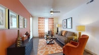 This single-floor residence is defined by a cohesive warm color palette of terracotta, rust, and cream tones that carry throughout the space, creating a bold and inviting ambiance. The living room serves as a central gathering area, featuring wood-style flooring, a ceiling fan, and large windows dressed with vibrant patterned curtains that fill the room with natural light. The open-concept kitchen is a standout feature, showcasing dark espresso cabinetry, granite countertops, a mosaic tile backsplash, and a full suite of stainless steel appliances. A generous breakfast bar with pendant lighting and bar stool seating connects the kitchen seamlessly to the living and dining areas, making it ideal for entertaining. The bedroom offers a comfortable retreat with plush carpeting, a ceiling fan, ample closet space, and a window with natural light. The bathrooms are finished with dark vanity cabinetry, granite countertops, and a tub-shower combination with tile surround. A dedicated laundry area houses a full-size top-loading washer and dryer, adding everyday convenience. Throughout the residence, consistent design choices in fixtures, finishes, and accent colors tie each space together cohesively.