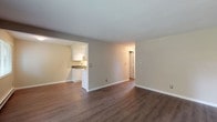 This single-floor unit offers a clean, functional layout designed for comfortable everyday living. The open living area serves as the heart of the space, featuring warm hardwood-style flooring, neutral beige walls, and a textured ceiling that add to its understated character. A sliding glass door floods the room with natural light and provides direct access to a private balcony overlooking lush greenery, creating a seamless indoor-outdoor connection.

Adjacent to the living area, the galley-style kitchen is efficiently designed with white cabinetry lining both sides, dark countertops, a single-basin sink, and a full suite of white appliances including a refrigerator, electric range, and microwave. Track lighting overhead ensures the kitchen is well-lit throughout the day.

The two bedrooms are carpeted for comfort and feature baseboard heating, neutral tones, and windows with slatted blinds that allow natural light while maintaining privacy. The views of surrounding trees give both rooms a peaceful, nature-connected feel.

The bathroom is neatly appointed with white cabinetry, a dark countertop vanity with an undermount sink, and a full tub-shower combination. Hardwood-style flooring carries through into this space, tying the overall aesthetic together. Clean white trim and consistent finishes throughout lend the unit a cohesive, move-in-ready appeal.
