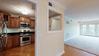 This single-floor residence offers a thoughtfully designed layout accommodating two bedrooms and two full bathrooms. The kitchen is a functional highlight, featuring rich wood cabinetry with raised-panel detailing, dark granite countertops, and a full suite of stainless steel appliances including a gas range, built-in microwave, dishwasher, and refrigerator. Hardwood-style flooring runs through the kitchen and connecting hallways, adding warmth throughout. A distinctive interior pass-through window connects the kitchen area to the adjacent living space, enhancing openness.

The bedrooms are generously proportioned, finished with plush carpeting and warm neutral wall tones. The primary bedroom connects directly to a walk-in closet equipped with wire shelving and hanging rods, as well as an en-suite bathroom. This bathroom features a wood vanity with granite countertop, a separate glass-enclosed shower, tile flooring, and classic subway tile wainscoting with a contrasting dark accent border. The second bathroom offers a tub-shower combination with matching white subway tile and chrome fixtures. A window in the second bedroom frames a pleasant outdoor view.