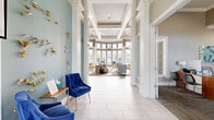 Located at 10500 Irma Dr in Northglenn, Colorado, this thoughtfully designed single-floor community space offers an inviting and vibrant atmosphere throughout. The grand entrance hallway immediately impresses with soaring ceilings, large grid-pane windows that flood the space with natural light, crisp white columns, and teal accent walls adorned with botanical wall art — setting an elegant, welcoming tone.

The primary living area is a showstopper, featuring dramatic double-height ceilings with clerestory windows, a striking floor-to-ceiling chevron-tiled fireplace surround, and abundant outdoor views. Patterned carpeting, teal and gold accent chairs, and vibrant artwork contribute to the room's upscale, curated ambiance. An adjacent lounge area offers additional seating with patterned carpeting, recessed lighting, a large wall-mounted TV, bold navy and colorful artwork, and comfortable sectional seating — ideal for social gatherings.

A media room with wall-mounted TV, built-in cabinetry, and a snack bar provides a dedicated entertainment space. The kitchen features warm wood cabinetry, a glass mosaic tile backsplash in cool blues and grays, stone countertops, stainless steel appliances, and a window that brings in natural light. Three connecting hallways ensure smooth flow between all areas, making this a highly functional and visually dynamic communal destination.