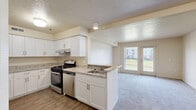 Located at 1234 Farm Crest Cir in Mishawaka, Indiana, this single-story unit presents a clean, functional layout designed for comfortable everyday living. The kitchen serves as a central feature, outfitted with white shaker-style cabinetry extending to the ceiling for ample storage, light granite-look countertops, and a full suite of stainless steel appliances including a gas range, dishwasher, and refrigerator. Wood-look plank flooring runs throughout the kitchen, grounding the bright, neutral palette. A peninsula with an integrated sink connects the kitchen to the adjacent living area, creating an open, cohesive flow between the two spaces.

The living area is carpeted and bathed in natural light through a large window and a rear-access door that opens to an outdoor view of the surrounding grounds. The textured ceiling and neutral wall tones carry throughout the unit, maintaining a consistent, understated aesthetic.

The bedroom features plush carpet, dual windows with horizontal blinds allowing generous natural light, and a closet with louvered bifold doors. Additional rooms include a secondary carpeted space suitable for a bedroom or flexible use, and a bathroom with wood-look flooring, a white vanity with granite-look counters, a tub-shower combination, and chrome hardware accents throughout.
