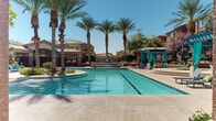 Located at 9745 Grand Teton Dr in Las Vegas, NV, this single-level outdoor amenity space showcases a resort-inspired design with warm terracotta and stucco architecture that reflects the Southwest's desert aesthetic. The centerpiece is a generously sized swimming pool with a dedicated lap lane, framed by towering palm trees and a decorative fountain feature that adds a tranquil ambiance to the sun-drenched surroundings. Adjacent to the pool, a bubbling spa sits beneath a teal-accented pergola, complemented by Adirondack seating and lush landscaping. A fully equipped outdoor kitchen provides a stainless steel grill, granite countertops, and a sink beneath a covered pavilion, making it ideal for gatherings. Multiple covered lounge areas feature ceiling fans, comfortable seating including daybed-style sofas and hanging egg chairs, and a fireplace-equipped pavilion with a mounted television for outdoor entertainment. The gated entryway with decorative columns provides a welcoming, secure entrance to the space. A water fountain and restroom access ensure convenience for guests. Throughout, the wide concrete pool deck offers ample space for sunbathing, while vibrant landscaping and natural light create an inviting, resort-like atmosphere year-round.