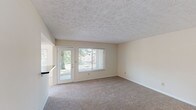 This single-floor unit on Tanager Drive in Burlington, Kentucky, offers a straightforward, functional layout with a clean, neutral aesthetic throughout. The living area is generously proportioned, featuring wall-to-wall carpeting in a warm beige tone, cream-colored walls, and a textured ceiling. Large sliding windows and a glass-paneled exterior door flood the space with natural light and provide outdoor views of mature trees and the surrounding neighborhood, contributing to an open and airy atmosphere.

The galley-style kitchen is efficiently arranged, featuring warm wood cabinetry with ample upper and lower storage, dark countertops, a stainless steel sink, and white appliances including a refrigerator, electric range, built-in microwave, and dishwasher. Tile flooring runs through the kitchen, providing a durable, easy-to-maintain surface that contrasts with the carpeted living spaces.

The bedrooms continue the consistent neutral palette, each equipped with carpeted floors, cream walls, a textured ceiling, and windows fitted with blinds for natural light and privacy. The bathroom features a vanity with a wide mirror, dark countertop, wood cabinetry below, and tile flooring, offering a practical and tidy finish. Overall, the unit presents a cohesive, low-maintenance environment.