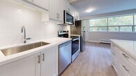 Located at 1640 Lawrence Ave W in Toronto's Lawrence Heights neighbourhood, this thoughtfully updated 2-bedroom, 1-bathroom unit offers a functional and modern living experience across a well-proportioned single floor. The open entrance flows into a generous living room—one of the largest areas in the unit—bathed in natural light through a wide band of windows that frame leafy, tree-lined outdoor views. Light wood laminate flooring runs throughout, lending a clean and cohesive aesthetic to every room. The kitchen has been fully renovated with crisp white shaker-style cabinetry, white subway tile backsplash, quartz countertops, and a full suite of stainless steel appliances including a range, over-the-range microwave, dishwasher, and refrigerator. A peninsula counter connects the kitchen to the open living area. Both bedrooms are well-sized, featuring the same light flooring, neutral walls, and windows with views of surrounding greenery. The bathroom is finished with classic white subway tile surrounding a soaker tub and shower combination. Additional highlights include multiple closets, in-unit laundry, and a private balcony—providing practical storage and outdoor space for everyday living.