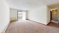Located at Fleetwood Drive in Waukesha, Wisconsin, this two-bedroom, two-bathroom unit is laid out on a single floor, offering a practical and functional living space. The open living room is carpeted and filled with natural light through a sliding glass door fitted with vertical blinds, which leads to an outdoor view and provides a bright, airy atmosphere. Baseboard heating is present throughout the unit, ensuring comfort year-round.

The galley-style kitchen features warm oak cabinetry extending to the ceiling for generous storage, a double sink with laminate countertops, wood-look vinyl flooring, and white appliances including a refrigerator and range. It connects seamlessly to the living area, which also offers a view into the kitchen with a ceiling fan overhead.

Both bedrooms are carpeted and bathed in natural light from large windows with blinds. The primary bedroom is a well-proportioned space featuring dual windows and a baseboard heater, while the second bedroom includes a louvered bifold closet door. The bathrooms include one with a full tub-and-shower combination adorned with white tile and gold accent squares, and another with a wide vanity, marble-patterned countertop, and a large wall mirror with a lighted fixture above.