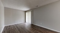 Located at 7929 Sycamore Ave in Kansas City, MO, this single-story 1-bedroom, 1-bathroom home offers a practical and well-appointed layout across a comfortable footprint. The living room features dark vinyl plank flooring, neutral gray walls, a textured ceiling, and vertical blinds covering a sliding door that provides outdoor access and natural light. An open passage connects to the dining area, which includes a ceiling fan and flows directly into the galley-style kitchen. The kitchen is outfitted with white shaker cabinets, dark countertops, a matte black faucet, and black appliances including a refrigerator, range, microwave, and dishwasher, all set over light wood-tone vinyl plank flooring. The bedroom is carpeted, offering a quieter, softer underfoot feel, and features a large window with outdoor views, plus a dedicated alcove housing a stacked washer and dryer unit for added convenience. The hallways connecting the rooms are finished with light wood-tone vinyl plank flooring, maintaining a cohesive aesthetic throughout. The bathroom includes large-format gray tile surrounding a full tub and shower, with matte black fixtures and a clean, contemporary finish. Textured ceilings are consistent throughout the home.