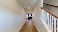 This two-story home is thoughtfully designed with a consistent, modern aesthetic carried throughout both levels. The main floor opens through a generous hallway finished with warm hardwood-style flooring and crisp white baseboards, leading directly into an open-concept kitchen and living area. The kitchen serves as a focal point, featuring dark espresso cabinetry, light granite countertops, a central island with pendant lighting, and black appliances, including a refrigerator and range. Recessed lighting and natural light from front-facing windows illuminate the space effectively. The living area extends from the kitchen, offering an open and flexible layout with access to an exterior door framed by additional windows.

The staircase, positioned adjacent to the main hallway, features a classic design with white balusters, an oak handrail, and a sturdy newel post, transitioning to carpeted treads on the way up. The upper level includes spacious bedrooms with plush carpeting and multiple windows providing natural light. The primary bedroom is accompanied by a walk-in closet outfitted with wire shelving. The primary bathroom presents a double-sink vanity with granite countertops and dark cabinetry, while a secondary bathroom includes a tub-shower combination with matching granite and tile finishes.