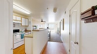 This single-floor, 3-bedroom, 2-bathroom home offers a well-designed layout that maximizes every inch of its compact footprint. The open-concept kitchen and living area serves as the heart of the home, where warm wood-look flooring flows from the kitchen into the main corridor. The kitchen is equipped with white cabinetry featuring wood-tone trim, a full-size refrigerator, electric range, and a peninsula counter that separates the cooking area from the living space. A ceiling fan overhead adds comfort to the area. Conveniently tucked within the kitchen is an in-unit laundry closet housing a full washer and dryer. The living room is bright and welcoming, featuring plush carpet, warm-toned walls, and a large sliding glass door that opens to a private balcony with open scenic views, allowing abundant natural light to fill the space. A carpeted hallway connects the three bedrooms and two bathrooms. The primary bedroom offers a ceiling fan and a sliding-door closet. Both bathrooms feature wood-look flooring, vanities with countertop sinks, and shower-tub combinations. The overall ambiance is clean, functional, and comfortable, making this home a practical and inviting living space.