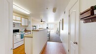 This single-floor, 3-bedroom, 2-bathroom home offers a well-designed layout that maximizes every inch of its compact footprint. The open-concept kitchen and living area serves as the heart of the home, where warm wood-look flooring flows from the kitchen into the main corridor. The kitchen is equipped with white cabinetry featuring wood-tone trim, a full-size refrigerator, electric range, and a peninsula counter that separates the cooking area from the living space. A ceiling fan overhead adds comfort to the area. Conveniently tucked within the kitchen is an in-unit laundry closet housing a full washer and dryer. The living room is bright and welcoming, featuring plush carpet, warm-toned walls, and a large sliding glass door that opens to a private balcony with open scenic views, allowing abundant natural light to fill the space. A carpeted hallway connects the three bedrooms and two bathrooms. The primary bedroom offers a ceiling fan and a sliding-door closet. Both bathrooms feature wood-look flooring, vanities with countertop sinks, and shower-tub combinations. The overall ambiance is clean, functional, and comfortable, making this home a practical and inviting living space.