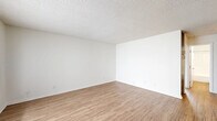Located at 3454 Ruffin Rd in San Diego, CA, this single-floor, 3-bedroom, 2-bathroom home offers a functional and well-appointed layout. The open living room features warm wood-look flooring, crisp white walls, and a large window with vertical blinds that fills the space with natural light. The kitchen is outfitted with two-tone cabinetry — dark lower cabinets contrasting with white uppers — along with stainless steel appliances including a refrigerator, range, and dishwasher, plus a skylight-style overhead fixture and a window above the sink. The two bathrooms are finished with wood-look flooring; one includes a glass-door walk-in shower with a dark vanity, while the other offers a full tub-shower combination with chrome fixtures. The three bedrooms are carpeted and bright, each with windows dressed in horizontal blinds. The spacious primary bedroom features a mirrored sliding-door closet with built-in shelving, maximizing both storage and the sense of space. A textured ceiling is consistent throughout the home, adding a classic residential character. The hallway connects all rooms efficiently, completing this practical and comfortable San Diego home.