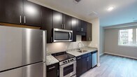 Located at 1703 Cresthill Ave in Royal Oak, Michigan, this single-floor unit offers a thoughtfully designed layout with modern finishes throughout. The kitchen is a standout feature, showcasing rich dark espresso cabinetry that extends to the ceiling for ample storage, complemented by light granite countertops and a full suite of stainless steel appliances including a refrigerator, electric range, over-the-range microwave, and dishwasher. Light wood-tone luxury vinyl plank flooring runs consistently throughout the space, creating a cohesive and clean aesthetic. The open living area flows naturally from the kitchen, offering a bright and versatile space with neutral gray walls and recessed lighting. The bedroom is generously proportioned, featuring a sliding barn-style door that opens to a dedicated laundry area with stacked washer and dryer, as well as access to additional closet space. The bathroom is finished with dark large-format tile surrounding the soaking tub and shower, paired with granite countertops on the vanity, wood-tone flooring, and chrome fixtures. The overall design balances contemporary style with functional living, making this a well-appointed and move-in-ready space in the heart of Royal Oak.