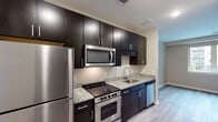 Located at 1703 Cresthill Ave in Royal Oak, Michigan, this single-floor unit offers a thoughtfully designed layout with modern finishes throughout. The kitchen is a standout feature, showcasing rich dark espresso cabinetry that extends to the ceiling for ample storage, complemented by light granite countertops and a full suite of stainless steel appliances including a refrigerator, electric range, over-the-range microwave, and dishwasher. Light wood-tone luxury vinyl plank flooring runs consistently throughout the space, creating a cohesive and clean aesthetic. The open living area flows naturally from the kitchen, offering a bright and versatile space with neutral gray walls and recessed lighting. The bedroom is generously proportioned, featuring a sliding barn-style door that opens to a dedicated laundry area with stacked washer and dryer, as well as access to additional closet space. The bathroom is finished with dark large-format tile surrounding the soaking tub and shower, paired with granite countertops on the vanity, wood-tone flooring, and chrome fixtures. The overall design balances contemporary style with functional living, making this a well-appointed and move-in-ready space in the heart of Royal Oak.