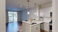 This well-appointed single-floor residence offers a thoughtfully designed open-concept layout that seamlessly connects the kitchen, dining, and living areas. The kitchen is a standout feature, equipped with stainless steel appliances including a gas range, over-the-range microwave, refrigerator, and dishwasher. White shaker-style cabinetry, a subway tile backsplash, and light quartz countertops lend a clean, contemporary aesthetic. A peninsula with an undermount sink and pendant lighting above creates a natural division between the kitchen and the living space, while also providing casual seating and additional prep space. Track lighting further illuminates the open area.

The living room is bright and airy, featuring warm hardwood flooring and a sliding glass door that opens to a private balcony with views of surrounding greenery, allowing generous natural light to fill the space. The bedrooms are finished with plush carpeting and neutral tones, offering a calm and comfortable retreat. One bedroom features a large window with outdoor views.

The bathroom is clean and functional, offering a full tub-shower combination with tiled surround, a single-sink vanity with ample cabinet storage, and hardwood-style flooring. A stacked laundry unit is also conveniently located within the residence. Overall, the space presents a modern, neutral palette throughout.