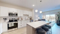 Located at 7956 Rose St in Victoria, MN, this 1-bedroom, 1-bathroom residence offers a thoughtfully designed single-floor layout that maximizes both function and comfort. The open-concept kitchen and living area serves as the heart of the home, featuring white shaker-style cabinetry, a subway tile backsplash, stainless steel appliances, and a large center island with pendant globe lighting overhead — ideal for cooking and casual dining. Light hardwood-style flooring runs throughout the main living areas, enhancing the bright, airy atmosphere. The living room flows seamlessly to a private balcony through a full-width sliding glass door, filling the space with natural light and offering outdoor views. The bedroom is carpeted for comfort, includes a window for additional natural light, and features dedicated closet space. The full bathroom is finished with warm wood-toned cabinetry, a white countertop vanity, and a tub-shower combination. Additional conveniences include an in-unit laundry room and a utility room. Neutral tones and clean finishes throughout create a cohesive, modern aesthetic well-suited for everyday living.