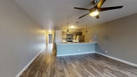 This single-floor unit offers a thoughtfully designed open-concept layout where the living area flows seamlessly into the kitchen. Durable hardwood-style flooring runs throughout the space, complemented by neutral gray tones on the walls and clean white baseboards that create a cohesive, modern aesthetic.

The kitchen is equipped with a full suite of stainless steel appliances, including a refrigerator, electric range, and over-the-range microwave. Dark cabinetry contrasts elegantly with light quartz-style countertops, while a hexagonal mosaic tile backsplash adds a distinctive design touch. Pendant lighting and a ceiling-mounted track light illuminate the kitchen, which opens to the living area via a raised breakfast bar. A ceiling fan with an integrated light fixture serves the main living space, which also benefits from a large front-facing window that draws in natural light.

The primary bedroom includes a ceiling fan, a sliding glass door leading to an outdoor area, and access to a built-in shelving closet. An additional bedroom features darker hardwood-style floors and neutral walls. The bathroom is finished with a gray vanity, a framed mirror, and a standout marble-look tiled tub and shower surround that serves as a focal point of the room.