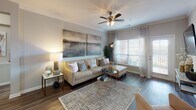 Located at Integra Springs in Kannapolis, NC, this single-floor residence offers a thoughtfully designed layout that balances comfort and functionality. The living room is a welcoming focal point, showcasing rich hardwood-style flooring, crown molding, a ceiling fan with light fixture, and generous windows dressed with sheer curtains that invite abundant natural light. A dedicated dining nook adds charm with its intimate scale and tasteful wall accents.

The kitchen is equipped with dark espresso cabinetry, light stone countertops, a tile backsplash, and black appliances, including a range and built-in microwave. A convenient in-unit laundry area is accessible directly from the kitchen.

Multiple bedrooms provide comfortable retreats, each featuring plush carpeting and ample closet space. One bedroom includes a walk-in closet with built-in shelving. The bedrooms are finished with neutral tones that create a calm, restful atmosphere.

Two full bathrooms mirror the kitchen's design aesthetic, featuring dark wood vanities, light countertops, large mirrors, tile flooring, and tub-shower combinations with tile surrounds. The overall palette throughout the residence is a cohesive blend of warm neutrals and deep wood tones, lending the space a polished, contemporary character.