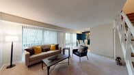This two-floor residence offers a well-organized layout designed for comfortable living. The main level centers around a spacious living room filled with natural light from large floor-to-ceiling vertical blind-covered windows and a sliding glass door that opens to an outdoor area. The open floor plan connects the living room to a dedicated dining space, which features a bold teal accent wall and decorative wall art, creating a visually distinct and inviting area for meals. A staircase with a clean white railing leads to the upper level. The kitchen is efficiently designed with warm oak cabinetry, ample counter space, and a full suite of white appliances including a gas range, dishwasher, and refrigerator, complemented by light wood-style flooring. The bedrooms are carpeted and offer a calm, restful atmosphere. The primary bedroom includes a closet and is accented by a cool grey feature wall, while additional bedrooms provide closet storage and natural light from exterior-facing windows with views of surrounding greenery. The bathroom is finished with wood-toned cabinetry, a tub-shower combination, and wood-style flooring, completing this thoughtfully arranged multi-level home.