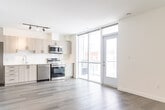 Located at 388 King Street in downtown Kitchener, Ontario, this modern 2-bedroom, 1-bathroom unit offers a thoughtfully designed open-concept layout finished with light hardwood-style flooring and crisp white walls throughout. The kitchen is a standout feature, equipped with stainless steel appliances including a refrigerator, electric range, dishwasher, and microwave, complemented by light wood cabinetry, a white tile backsplash, and a clean-lined countertop with an undermount sink. Floor-to-ceiling windows flood both the kitchen and living area with natural light while providing views of the surrounding streetscape. The open living room flows seamlessly from the kitchen, offering a versatile and bright space. Two bedrooms provide comfortable accommodations, with the primary bedroom benefiting from a dedicated window that brings in natural daylight and neighbourhood views. The second bedroom is a well-proportioned, quiet space. The bathroom is finished with large-format neutral stone-look tile surrounding a soaker tub and shower combination, paired with chrome fixtures for a clean, contemporary aesthetic. A hallway connects all rooms efficiently, contributing to the unit's functional and modern design.