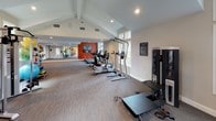 Located at 3400 Sweetwater Rd in Lawrenceville, GA, this single-level fitness center is designed to offer a comprehensive and motivating workout environment. The space is defined by its striking vaulted ceilings with exposed beams, which lend an open, airy quality throughout the main exercise floor. Recessed lighting complements the abundant natural light streaming in through large, multi-pane windows that frame lush green outdoor views, creating a bright and energizing atmosphere.

The cardio zone features a row of True-brand treadmills and elliptical machines positioned along the windowed walls, allowing users to enjoy the scenic surroundings during workouts. The strength training area is well-appointed with Freemotion cable machines, multi-function weight stations, adjustable benches, and a variety of functional training accessories including resistance bands and stability balls. A full-length mirror accent wall enhances the sense of space in the main exercise area.

A bold typographic fitness-themed mural anchors one end of the room, adding visual energy and reinforcing the motivational atmosphere. The facility is finished with durable, textured carpet flooring throughout, and features a dedicated entrance with glass double doors. The overall design balances functionality with an inviting aesthetic, making it a well-rounded community fitness facility.