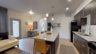 This well-appointed single-floor residence offers a thoughtfully designed open-concept layout that seamlessly connects the kitchen, dining, and living areas. The kitchen is a standout feature, showcasing dark espresso cabinetry, a white subway tile backsplash, stainless steel appliances, and a generously sized granite-topped island with bar seating for multiple guests — ideal for both everyday meals and entertaining. Recessed and pendant lighting illuminate the space, which is finished with light wood-look flooring throughout the main areas.

The living room is a comfortable and inviting retreat, featuring a ceiling fan, natural light from a large window with draping curtains, and ample room for a sectional sofa and accent furnishings. A dedicated workspace or dining nook adds functional versatility to the open floor plan.

The two bedrooms are carpeted for warmth and comfort. The primary bedroom includes a walk-in closet and a window that brings in natural light, while the secondary bedroom offers a cozy, well-organized layout. Both full bathrooms are finished with wood-look tile flooring, dark cabinetry with granite countertops, and a shower-tub combination, presenting a clean and cohesive aesthetic throughout the home.