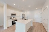 Located at 100 Oakbrook Drive in McDonough, GA, this single-story 2-bedroom, 2-bathroom home offers a clean, modern design with a bright and open layout. The combined kitchen and living area serves as the heart of the home, featuring a large center island with an undermount sink, crisp white shaker cabinetry, light quartz countertops, and a full suite of stainless steel appliances including a French door refrigerator, electric range, and over-the-range microwave. Recessed lighting illuminates the space, which flows seamlessly into the living area. Light wood-style flooring runs consistently throughout the home, contributing to a cohesive and contemporary aesthetic. A dedicated pantry provides additional storage adjacent to the kitchen. Both bedrooms are well-proportioned and bathed in natural light from large windows that frame views of surrounding trees, with ceiling fans adding comfort. The primary bedroom connects to a private bathroom featuring a white vanity with dual sinks and a walk-in closet equipped with wire shelving. A utility room and multiple closets offer practical storage solutions throughout. The living area opens to a sliding glass door with vertical blinds, bringing in generous natural light and outdoor greenery views.