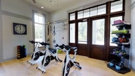 Located at 100 Underwood Dr in Summerville, South Carolina, this single-floor fitness facility is designed to support an active and health-focused lifestyle. The space is thoughtfully appointed with dedicated exercise equipment, including a row of professional-grade spinning bikes and TRX suspension training straps mounted to a wall-mounted rack system — ideal for both cardio and functional strength training.

Large windows line the walls, flooding the interior with abundant natural light and offering pleasant views of the surrounding greenery. The prominent dark-wood double entry doors with glass panels add a polished, welcoming aesthetic while maintaining a visual connection to the outdoors. Light hardwood flooring runs throughout the space, contributing to a clean, airy atmosphere that complements the bright, white walls and recessed lighting above.

The layout is open and well-organized, providing ample room to move freely between equipment stations. Additional fitness accessories, such as weighted discs and training aids, are neatly stored and accessible. The overall ambiance is bright, functional, and motivating — creating an inviting environment well-suited for a community fitness or wellness center.