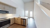 Located on Vanowen Street in Canoga Park, Los Angeles, this two-story unit showcases a thoughtfully designed interior with modern finishes throughout. The main living level immediately impresses with dramatically high ceilings that amplify the sense of openness, while wood-style flooring runs throughout the main areas, grounding the bright, airy atmosphere.

The kitchen is well-appointed with light wood cabinetry extending to near ceiling height, complemented by a clean white subway tile backsplash and sleek quartz countertops. Stainless steel appliances — including a refrigerator, range, built-in microwave, and dishwasher — are seamlessly integrated into the design. The kitchen opens toward the living area, which benefits from natural light and direct access to a private balcony through a glass door.

The upper level features carpeted bedroom spaces with ample closet storage, accessible via a staircase with white-painted railings. The bedroom area opens to a loft-style layout overlooking the lower level. A full bathroom includes large-format tile surrounds, a soaking tub, and wood-look flooring. A dedicated in-unit laundry closet with a stacked washer and dryer adds everyday convenience to this well-finished, multi-level space.