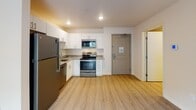 Located at 9844–9930 59th Ave N in Plymouth, Minnesota, this single-floor unit offers a clean, modern interior with a thoughtfully designed open layout. Light-toned luxury vinyl plank flooring runs throughout, lending a cohesive and contemporary feel to the space.

The living area is bright and open, with neutral warm-beige walls and a textured ceiling. A sliding glass door leads to a private balcony with a metal railing, allowing natural light to fill the room and providing an outdoor retreat. A built-in HVAC panel is integrated neatly into the wall, maintaining a streamlined aesthetic.

The kitchen is efficiently arranged and well-equipped, featuring white cabinetry, granite-style countertops, and a full suite of stainless steel appliances including a refrigerator, electric range, microwave, and dishwasher. Recessed lighting overhead enhances the functionality of the space.

The bathroom is clean and practical, with wood-look flooring, a single-sink vanity topped with a granite-style countertop, white cabinetry with brushed nickel hardware, a large mirror with overhead lighting, and a tub-shower combination. The layout flows logically from the living and kitchen areas into the private spaces, creating an organized and comfortable single-floor residence.