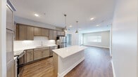 Located at 6276 Newton Rd in Haslett, MI, this well-designed 2-bedroom, 4-bathroom residence offers a thoughtfully planned single-floor layout. The open-concept kitchen and living area forms the heart of the home, showcasing warm hardwood-style flooring, recessed lighting, and a generous central island topped with a crisp quartz countertop. Stylish pendant lights hang above the island, complementing the taupe cabinetry, subway tile backsplash, and a full suite of stainless steel appliances including a refrigerator, range, microwave, and dishwasher. The living area extends naturally from the kitchen, brightened by a large window and a glass-paneled door leading to a private balcony with outdoor views. The primary bedroom is a comfortable retreat with plush carpeting, and a dedicated walk-in closet with wire shelving for organized storage. A second bedroom features soft carpet and a distinctive horizontal clerestory window that introduces natural light while maintaining privacy. A dedicated laundry room houses a full-size washer and dryer. With four bathrooms, this residence provides ample convenience for residents and guests alike. The overall aesthetic is clean and contemporary, with neutral tones throughout.
