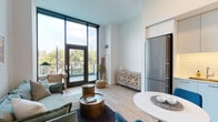 Located at 845 W Madison St in Chicago's dynamic West Loop neighborhood, this single-floor residence combines contemporary design with functional living. The open-concept layout connects the living, dining, and kitchen areas into a cohesive and well-lit space.

The living area is defined by dramatic floor-to-ceiling windows framed in dark trim, flooding the room with abundant natural light and offering treetop views of the surrounding cityscape. A glass door leads directly to a private balcony, extending the living space outdoors. Light wood-tone flooring runs throughout, complementing the bright white walls and creating a clean, modern aesthetic.

The kitchen is thoughtfully designed with sleek, light gray cabinetry extending to the ceiling, stainless steel appliances including a gas range, built-in microwave, and full-size refrigerator, as well as under-cabinet lighting and a subway tile backsplash. A compact dining area adjoins the kitchen, ideal for casual meals.

The entryway offers a welcoming transition with warm wood flooring and practical storage. The bathroom features large-format floor tiles, a walk-in shower with vertical tile, and a clean white vanity. An in-unit stacked Whirlpool washer and dryer provide added convenience.