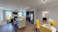 This single-floor residence offers a thoughtfully designed open-concept layout that seamlessly connects the kitchen, dining, and living areas. The kitchen is outfitted with dark espresso cabinetry, stainless steel appliances, and a granite-topped island with bar seating, illuminated by pendant lighting overhead. Crown molding adds a refined touch throughout the main living areas, which feature rich hardwood-style flooring.

The living room serves as a comfortable gathering space, centered around a stone-accented fireplace and complemented by a ceiling fan and multiple windows that invite natural light. An adjacent dining area provides additional seating in close proximity to the kitchen.

The primary bedroom is generously sized with plush carpeting, multiple windows with patterned drapes, and direct access to an en suite bathroom featuring a glass-enclosed walk-in shower and tile flooring. A second bedroom, also carpeted and well-lit, shares access to a full bathroom complete with a dark-cabineted vanity, tub-shower combination, and stone-style tile flooring. Throughout the residence, a consistent gray-and-yellow color palette creates a cohesive and contemporary ambiance.
