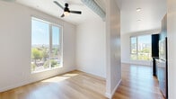 Located in Portland's vibrant NW district, this single-floor unit offers a thoughtfully designed layout with a clean, contemporary aesthetic. Light hardwood flooring runs throughout, complementing the crisp white walls and contributing to a bright, open atmosphere. Large floor-to-ceiling windows flood the living area with abundant natural light and frame impressive views of the Portland cityscape and surrounding hills, creating a strong visual connection to the urban environment outside.

An exposed industrial-style ventilation duct traverses the ceiling, adding an architectural accent that pairs well with the modern design. A ceiling fan with a sleek black finish enhances comfort in the main living area. The kitchen is equipped with stainless steel appliances—including a range, microwave, and dishwasher—alongside slate-toned cabinetry, white countertops, and a wood open shelf, delivering both functionality and style.

Toward the rear of the unit, a dedicated in-unit laundry area with a stacked washer and dryer provides added convenience. A coat closet with a wire rack and a wall-mounted thermostat are also present. The overall layout is compact yet efficient, making excellent use of the available space while maintaining a clean, uncluttered feel throughout.