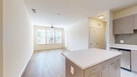 This 730-square-foot single-floor unit offers a well-designed layout with 2 bedrooms, 2 bathrooms, a combined kitchen and living room, and a closet. The modern kitchen is equipped with stainless steel appliances — including a refrigerator, range, microwave, and dishwasher — complemented by contemporary taupe cabinetry, quartz countertops, a mosaic tile backsplash, and light ceramic tile flooring. A kitchen island provides additional counter and prep space. The living room features warm hardwood-style flooring, crown molding, a ceiling fan, and large windows fitted with blinds that invite abundant natural light and views of surrounding greenery. The primary bedroom, at 130 square feet, continues the hardwood-style flooring, includes a ceiling fan, crown molding, a walk-in closet, and a bank of large windows overlooking outdoor scenery. The second bedroom features plush carpeting, a built-in closet with paneled double doors, and a window with natural light. Both bathrooms are finished with light ceramic tile flooring, tub-shower combinations with large white subway tile surrounds, and modern vanities with integrated sinks — one featuring a dark wood cabinet and the other with chrome fixtures.