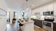 Located at 4454 Tropea Way in Jacksonville, Florida, this single-floor residence presents a thoughtfully designed open-concept layout that seamlessly connects the kitchen, dining, and living areas. The kitchen serves as a central highlight, featuring a generously sized island with granite countertops and seating, complemented by pendant globe lighting overhead. Cabinetry combines crisp white upper cabinets with rich dark lower cabinets, framing a subway tile backsplash. Stainless steel appliances — including a French door refrigerator, electric range with microwave, and dishwasher — complete the well-equipped space. Wood-look flooring flows throughout the main living areas, adding warmth and continuity.

The living room is bright and welcoming, benefiting from large windows and a glass-paned door that opens to a balcony, allowing abundant natural light and outdoor views. The bedrooms feature plush carpeting, large windows, and ample space. The bathroom is finished with granite countertops, dark wood cabinetry, a large mirror, and a walk-in closet with built-in shelving. An in-unit laundry area is also present. Overall, the space offers a clean, contemporary aesthetic with quality finishes throughout.