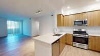 Located at 6513–6569 Sepulveda Blvd in Los Angeles, this single-floor residence presents a clean, modern aesthetic throughout. The kitchen serves as a central highlight, featuring warm honey-toned flat-front cabinetry, white quartz countertops, and a full suite of stainless steel appliances, including a gas range, built-in microwave, refrigerator, and dishwasher. A peninsula with an undermount sink extends into the living area, creating an open, connected layout ideal for both everyday living and entertaining. Light wood-look flooring runs continuously throughout the space, lending warmth and visual cohesion. The living area is bright and open, benefiting from recessed lighting and a seamless flow from the kitchen. Bedrooms are generously proportioned, filled with natural light from multiple windows, and include mirrored closet doors for added functionality. Two bathrooms mirror the home's design language, featuring wood-front vanities with white countertops; one includes a full soaking tub and shower combination with clean white tile surround, while the second offers a streamlined vanity setup. The overall ambiance is contemporary and light-filled, with a neutral palette that provides a versatile backdrop throughout.