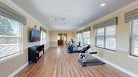 Located at 2400 NE 112th Ave in Vancouver, Washington, this well-appointed single-story community space offers a generous and thoughtfully designed floor plan. Throughout the facility, warm beige walls, crown molding, chair rail detailing, and durable hardwood-style flooring create a cohesive and inviting aesthetic.

The open common areas serve as the heart of the facility, featuring multiple dining and seating arrangements with dark wood tables and upholstered blue chairs. Ceiling fans and recessed lighting ensure a comfortable, well-lit environment. Decorative artwork and curated furnishings, including a bookshelf stocked with reading material, add warmth and a residential feel to the shared spaces.

The game room provides a dedicated area for recreation and social engagement, with card and game tables surrounded by comfortable seating. A fitness room, brightened by multiple windows with Roman shades offering views of the outdoors, is equipped with stationary bikes, a rowing machine, and additional exercise equipment, all set on hardwood-style flooring.

Two laundry rooms offer convenience, each featuring multiple washers and dryers, dark cabinetry, and light-toned countertops on tile flooring. Additional rooms provide quieter, more intimate settings with seating and glass-paneled doors, ideal for private meetings or small gatherings. The facility is designed to support an active and connected community lifestyle.
