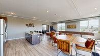 Located in Hastings, MN, this clubroom offers a thoughtfully designed communal space spread across a single floor. The open layout is anchored by light wood-look flooring, neutral gray walls, and exposed industrial ductwork that adds an urban, loft-inspired character throughout.

The lounge area serves as a central gathering point, featuring a leather sectional sofa, accent chairs, and a bold starburst-patterned area rug. A floor-to-ceiling tiled fireplace surround with a wall-mounted TV creates a striking focal point, lending warmth and sophistication to the seating area.

The kitchenette is equipped with dark wood cabinetry, granite countertops, a sink, and a dishwasher. A textured stone-look accent wall behind the counters adds visual depth, while a large granite-topped island provides additional prep and serving space. Decorative gear-motif wall art ties into the industrial aesthetic.

The gaming zone includes a full-length shuffleboard table, a pinball machine, and high-top tables with leather bar stools — ideal for social gatherings. Large windows flood the space with natural light and frame expansive views of the surrounding Hastings skyline and green landscape.

A glass door leads to a furnished outdoor terrace, extending the entertaining space and offering open-air enjoyment of the surrounding scenery.