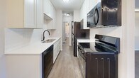 This 1-bedroom, 1-bathroom unit at 1001 Seventh Ave SW in Forest Lake, Minnesota offers a thoughtfully designed single-floor layout. The galley-style kitchen is a standout feature, equipped with sleek black stainless steel appliances including an electric range, over-the-range microwave, refrigerator, and dishwasher. Crisp white cabinetry pairs with light quartz countertops and a subway tile backsplash, creating a clean, modern aesthetic. Wood-look flooring runs throughout the unit, adding warmth and continuity across all rooms. The combined kitchen and living area is served by a ceiling fan with light kit, providing both comfort and functionality. A convenient in-unit stacked washer and dryer is tucked neatly within the space. The bedroom is comfortably sized, featuring a window that brings in natural light, a baseboard heating unit, and a full-width mirrored sliding closet that enhances the sense of space. Recessed accent lighting along the upper trim adds a modern touch to the living and bedroom areas. Neutral wall tones and textured ceilings complete the interior. The unit offers a practical and comfortable living environment in a residential neighborhood setting.