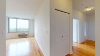This single-floor unit presents a clean, modern design throughout, characterized by crisp white walls, warm hardwood flooring, and an open, airy layout. The living and dining area is generously proportioned, flowing directly into a galley-style kitchen outfitted with dark espresso cabinetry, stainless steel appliances including a full-size refrigerator, oven, microwave, and dishwasher, and light-toned countertops over tile flooring.

Multiple bedrooms feature the same warm hardwood floors, white walls, and large picture windows that frame broad city views, filling each room with natural light. Each bedroom is well-sized, offering comfortable proportions and closet access.

The unit includes two bathrooms, both finished with dark vanity cabinetry, light countertops, and tile flooring. One bathroom features a tub-shower combination, while the other is equipped with a glass-enclosed walk-in shower. Both are clean and functional in design.

A hallway with a sliding door connects the unit's living spaces, providing clear separation between rooms. The overall aesthetic is contemporary and neutral, offering a versatile canvas throughout.