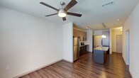 Located in Little Elm, this single-floor residence offers a thoughtfully designed open-concept layout that seamlessly connects the living and kitchen areas. Rich, dark hardwood-style flooring flows throughout the space, adding warmth and continuity to the interior. The living area is appointed with a contemporary ceiling fan, contributing both style and comfort to the room.

The kitchen is a standout feature, showcasing a full suite of stainless steel appliances, including a refrigerator, range, and built-in microwave. Medium-toned cabinetry provides ample storage, while a kitchen island topped with a light granite-style countertop serves as both a functional workspace and a casual gathering spot. Pendant lighting above the island adds a refined finishing touch.

Track lighting installed along the ceiling further enhances the modern aesthetic of the space, ensuring well-distributed illumination throughout. The clean white walls provide a neutral backdrop that complements the warm flooring and cabinetry tones. The open flow between the living and kitchen areas creates a spacious, airy feel, making the residence well-suited for both everyday living and entertaining. Overall, the space presents a polished, contemporary character with practical, high-quality finishes.