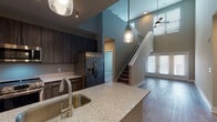 This two-story residence at 9200 Bruckhaus St in Raleigh, NC, offers a thoughtfully designed layout with modern finishes throughout. The main level centers around an open-concept kitchen and living area with soaring double-height ceilings that create a dramatic sense of volume. The kitchen is appointed with dark wood cabinetry, a granite-topped island with an undermount sink and pendant lighting, stainless steel appliances including a French door refrigerator, electric range, and microwave, along with a subway tile backsplash and hardwood-style flooring. A staircase connects the main level to the upper floor, where multiple carpeted bedrooms provide comfortable retreats. Each bedroom features ceiling fans, natural light from large windows with neighborhood views, and ample closet space. The primary suite includes an en-suite bathroom with a granite vanity, dark wood cabinetry, a glass-enclosed shower, and a walk-in closet. A secondary full bathroom features a soaking tub with tile surround and built-in shelving. A dedicated laundry space houses a full-size side-by-side GE washer and dryer. The upper level also includes a versatile open loft area with staircase access, ceiling fan, and exterior views, suitable for use as a flex space or secondary living area.