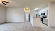 This single-story, one-bedroom, one-bathroom unit offers a thoughtfully designed layout that maximizes functionality within a compact footprint. The combined kitchen and living area creates an open, connected feel, with the kitchen featuring light wood-tone flooring, light gray cabinetry, white countertops, and stainless steel appliances including a range, microwave, and refrigerator. A peninsula-style counter separates the kitchen from the carpeted living area, which benefits from double French doors that invite natural light and provide outdoor access. A ceiling fan overhead adds both comfort and a finishing touch to the living space. The bedroom is a comfortable, well-proportioned room with soft carpeting, a ceiling fan, and a window with blinds that allows natural light to filter in. It includes access to a closet, offering practical storage. The bathroom is clean and efficient, featuring light wood-tone flooring, a single-sink vanity with gray cabinetry, and a tub-shower combination with tile surround. A dedicated laundry area houses a full-size top-load washer and dryer, adding significant everyday convenience. Throughout the unit, a neutral color palette of whites and soft grays creates a bright, cohesive, and move-in-ready atmosphere.