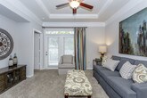 This single-floor residence offers a thoughtfully designed layout that balances comfort and functionality throughout its living spaces. The living room serves as the heart of the home, showcasing an elegant tray ceiling with crown molding and a ceiling fan, soft neutral-toned carpet, and a large window with French doors that invite natural light and outdoor views. A built-in niche adds architectural character to the space. The living area opens seamlessly to a breakfast bar with barstool seating, providing a natural transition into the galley-style kitchen. The kitchen features warm honey-toned cabinetry, granite-look countertops, a stainless steel sink, and a full suite of stainless steel appliances including a refrigerator and range. Rich, dark wood-look vinyl plank flooring runs the length of the kitchen, adding warmth and contrast. The bedrooms are generously sized, each finished with plush carpet and ample natural light from well-appointed windows dressed with blinds and drape panels. Ceiling fans provide comfort, and each room benefits from convenient closet access. The bathroom is cleanly finished with dark wood-look flooring, a tub-shower combination, and white cabinetry for storage. Throughout the residence, a cohesive neutral color palette and consistent finishes create a calm, welcoming ambiance.