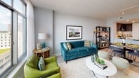 Located at 4850 Rugby Ave, Unit 101 in Bethesda, Maryland, this single-floor residence offers a thoughtfully designed open-concept layout with contemporary finishes throughout. Light-toned hardwood flooring runs seamlessly across the main living areas, lending a clean, modern aesthetic.

The kitchen is a standout feature, showcasing a striking two-tone cabinetry design with crisp white lower cabinets and rich dark wood upper cabinets. A marble-veined quartz peninsula provides generous counter space and casual seating, while stainless steel appliances — including a French door refrigerator, gas range, built-in microwave, and dishwasher — complete the chef-friendly setup. A textured white tile backsplash adds visual depth.

The open living area is bright and welcoming, with large floor-to-ceiling windows framing city views of the Bethesda skyline. Sheer drapes allow natural light to filter softly through the space, enhancing its airy ambiance. A dedicated dining area flows naturally from the kitchen, supporting both everyday living and entertaining.

The bathroom is finished with large-format white floor tiles and full subway tile surround in the tub-shower combination, maintaining the home's clean, neutral palette. Recessed lighting throughout the residence ensures well-illuminated spaces at every hour. Overall, the unit presents a polished, modern living environment in the heart of Bethesda.