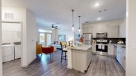 This single-floor residence features an open-concept layout that seamlessly integrates the kitchen, dining, and living areas into a cohesive, functional space. The kitchen is a standout feature, showcasing light-toned cabinetry, a bold navy tile backsplash, granite countertops, stainless steel appliances, and a central island with bar seating illuminated by sleek pendant lighting. Wood-look flooring flows throughout the main living areas, complementing the neutral, light-filled palette.

The living room benefits from large windows that invite natural light and outdoor views, while a ceiling fan adds both style and practicality. A dedicated dining area provides an intimate space for meals. The three bedrooms are carpeted for comfort, with the generously sized primary bedroom featuring windows that allow ample natural light. The two bathrooms are well-appointed; one includes a glass-enclosed walk-in shower with white tile surround, while the other offers a full soaking tub with a shower combination, granite-topped vanity, and wood-look flooring. The overall ambiance is modern, clean, and inviting throughout.