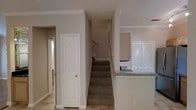 This two-story home offers a clean and comfortable layout with a cohesive neutral color palette throughout. The interior is finished with crisp white trim, crown molding, and light-toned walls that create a bright and welcoming atmosphere across both levels.

The main floor features light hardwood-style flooring that flows through the entryway and common areas. A central staircase with carpet treads connects the two floors, positioned conveniently near the heart of the home. Adjacent to the staircase is a paneled door that leads to a closet or utility area, adding practical storage to the main living space.

The kitchen is partially visible from the staircase area and features granite or stone-look countertops and louvered cabinet doors, lending a classic, timeless aesthetic. The open sightlines between the kitchen and the central hallway contribute to a connected, easy-flowing floor plan.

Crown molding is a consistent feature throughout the visible spaces, adding a refined architectural touch. The overall ambiance is light, airy, and well-kept, with a straightforward design that balances classic detailing with functional living. The neutral finishes throughout make the space highly versatile and move-in ready.