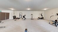 Located in Langley, BC, this dedicated exercise room offers a generously sized, single-floor fitness space designed to accommodate a variety of workout routines. The room features a clean, minimalist aesthetic with crisp white walls, neutral carpet flooring, and flush-mount ceiling lighting that creates a bright and welcoming atmosphere throughout.

The layout is open and well-organized, providing ample room to move between equipment. The cardio section is well-appointed with multiple elliptical trainers, stationary bikes — including both upright and recumbent models — and a rowing machine, catering to a range of cardiovascular preferences. A dedicated strength and functional training area includes a dumbbell rack with a variety of weights, a weight bench, and an assortment of fitness accessories such as resistance bands, a stability ball, and handheld weights in multiple sizes.

Structural columns punctuate the space without impeding the flow, while large windows along one wall allow natural light to filter in and offer views of the surrounding exterior. A full-length mirror near the entrance supports form and technique during workouts. Movable room dividers provide the flexibility to partition sections of the space as needed. An emergency exit door with clear signage ensures safety standards are met. The overall ambiance is functional, tidy, and purpose-built for active use.