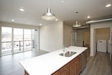 This well-appointed single-floor residence blends modern finishes with industrial design elements to create a functional and stylish living space. The kitchen serves as a focal point, featuring warm medium-toned wood cabinetry, a full suite of stainless steel appliances including a refrigerator, electric range, and over-the-range microwave, and a generous island with a white countertop and integrated sink. Exposed ductwork running along the ceiling adds a distinctive industrial character, complemented by pendant lighting in a barn-style design. Light wood-tone flooring runs throughout the main living areas, enhancing the bright and open atmosphere. The living area opens directly to a private balcony through large sliding glass doors, allowing for abundant natural light and outdoor views. The bedrooms are carpeted for comfort, each equipped with a ceiling fan. One bedroom features built-in shelving for added storage, while another offers a large window with exterior views. Two bathrooms are finished with matching wood-toned vanities, white countertops, and wood-look vinyl flooring. A dedicated in-unit laundry room houses a full-size washer and dryer, adding everyday convenience to this thoughtfully designed home.