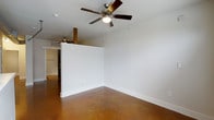 This studio is a well-designed single-floor space that makes efficient use of its footprint through a thoughtful open layout. The most striking feature is the polished concrete flooring, finished in warm amber and brown tones that lend an industrial yet inviting character throughout. Crisp white walls contrast beautifully with the rich flooring, creating a clean and modern aesthetic.

A partial dividing wall subtly separates the main living area from the additional zone beyond, offering a sense of spatial definition without fully enclosing the layout. This partition maintains an open, airy feel while providing a degree of functional zoning. Exposed wooden beam accents visible near the dividing wall add a rustic touch that complements the industrial concrete floors.

A ceiling fan with an integrated light fixture is centrally positioned in the main area, ensuring comfortable airflow and ambient lighting. A second ceiling fan is visible in the adjoining zone, reflecting consistent climate control throughout. The white walls and light-toned ceiling contribute to a bright, welcoming atmosphere. Overall, the studio balances industrial design elements with clean, minimalist finishes for a cohesive and practical living space.